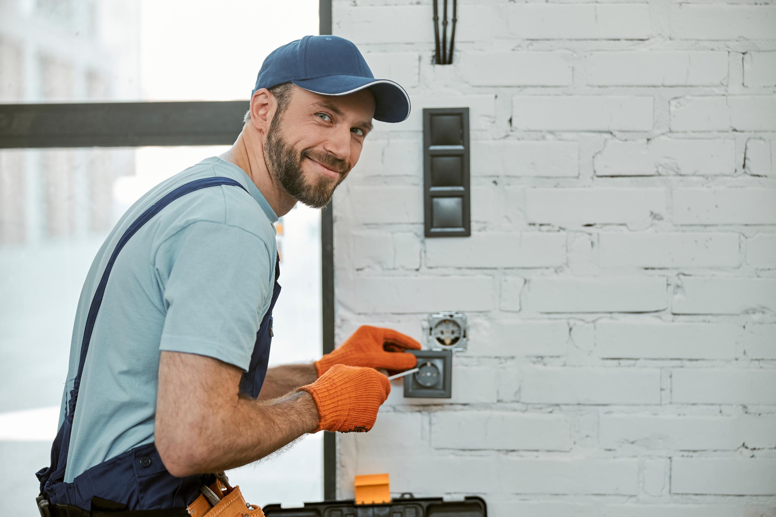 électricien souriant avec casquette réparant une prise électrique