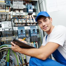 jeune électricien en bleu de travail et casquette devant armoire électrique