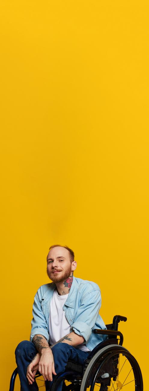 homme avec barbes et tatouages sur une chaise roulante, fond jaune
