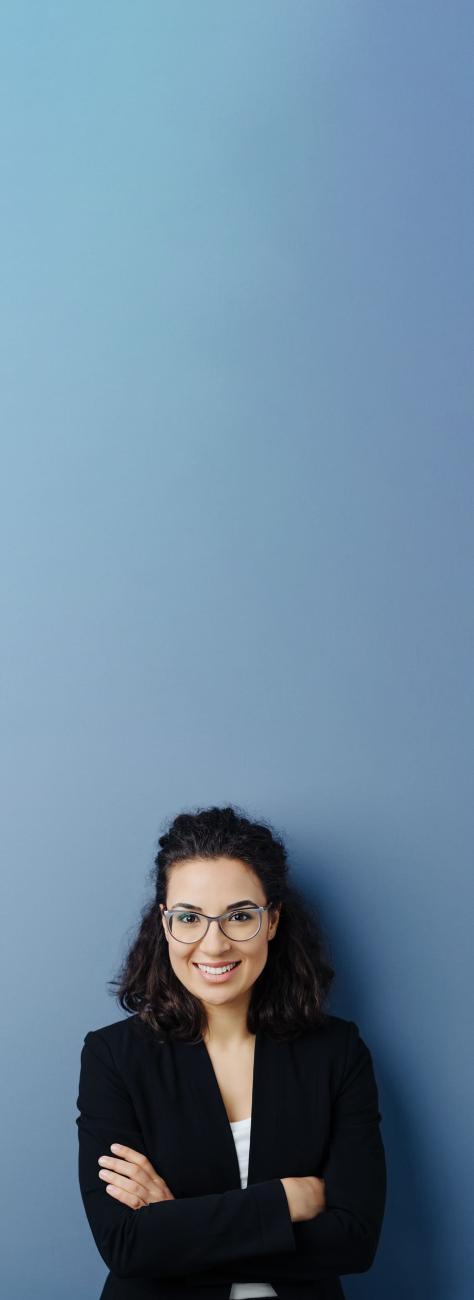 femme souriante avec tailleur noir et lunette, bras croisés, fond beu gris