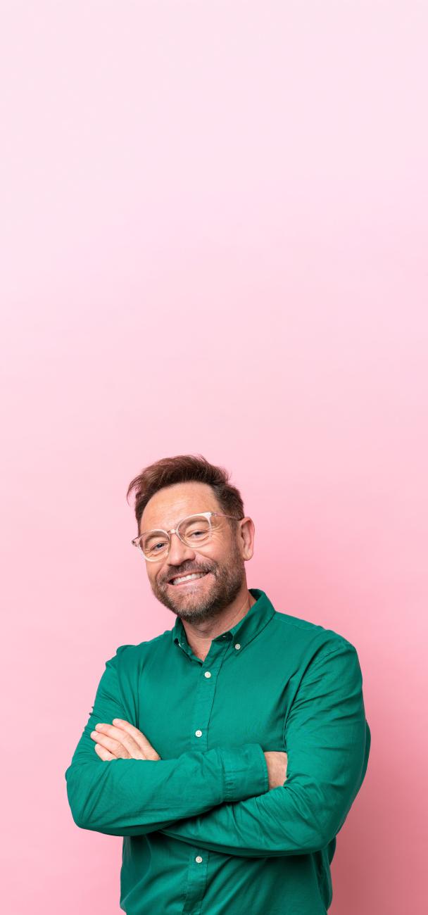 homme à lunette avec bras croisés sur fond rose