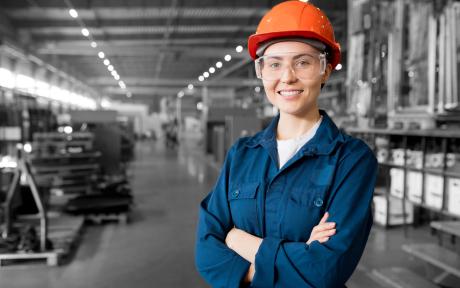 jeune alternante en bleu de travail et casque orange dans une usine