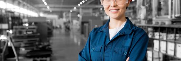 jeune alternante en bleu de travail et casque orange dans une usine