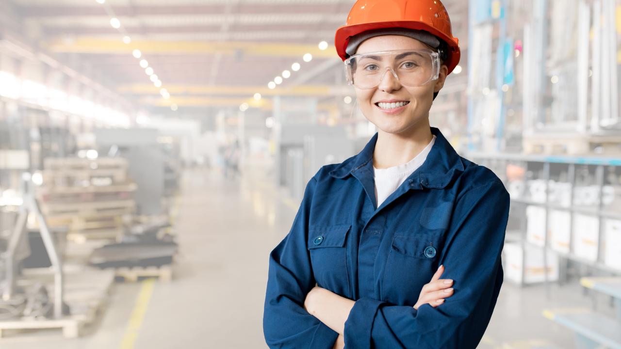 jeune femme en bleu de travail et casque orange dans une usine