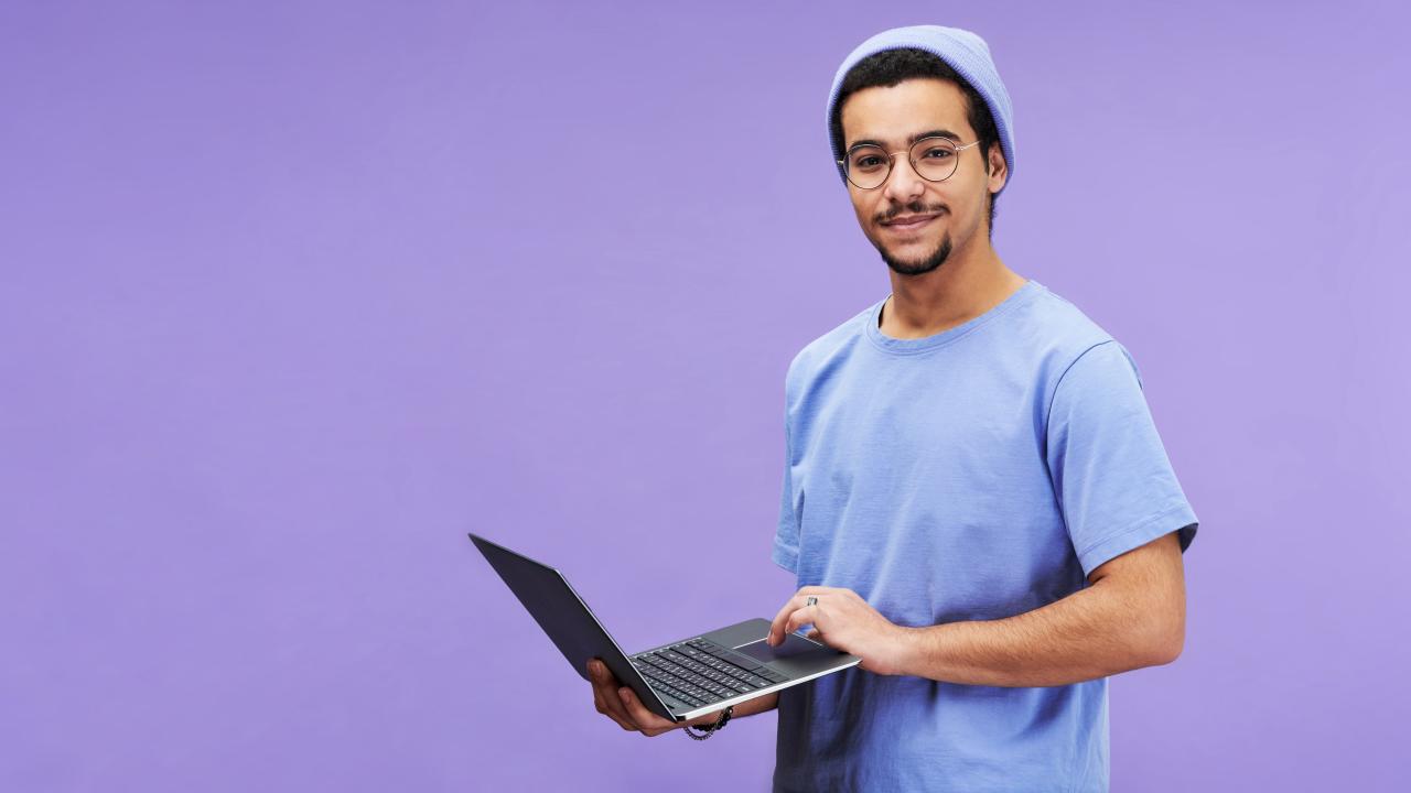 jeune avec bonnet tenant un ordinateur sur fond violet